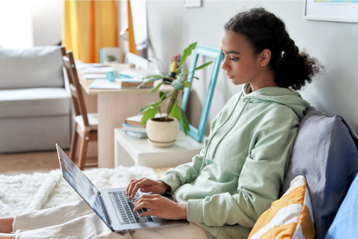 teen girl sitting on bed typing on computer