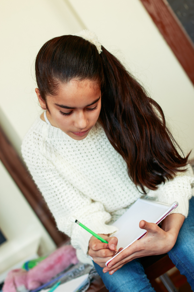 teen girl with a ponytail writing in a notebook